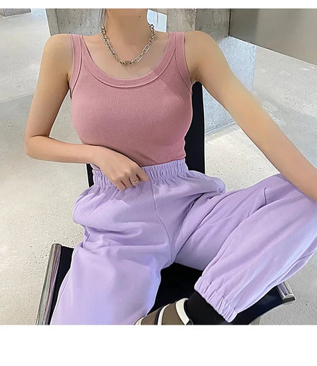 Model wearing a pink sleeveless ribbed tank top paired with lavender joggers in a modern indoor setting.
