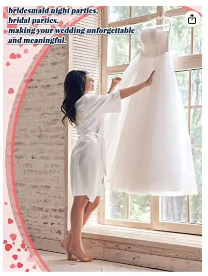 Woman in a satin robe admiring a white wedding dress by the window, perfect for bridal parties and making memories.