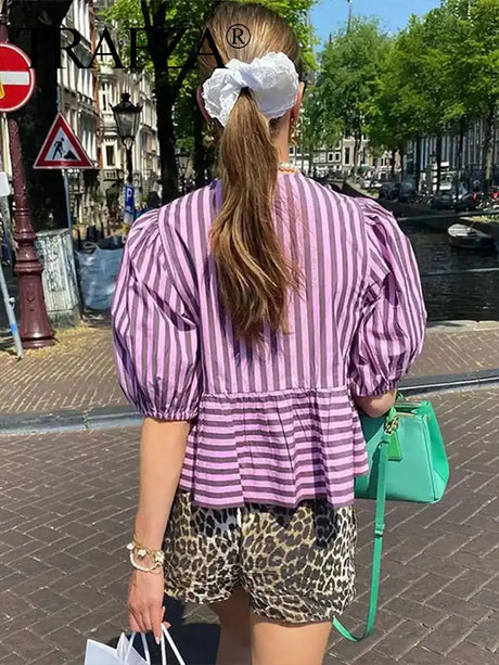 Woman wearing a striped lace-up blouse with puff sleeves, walking in a vibrant urban setting.
