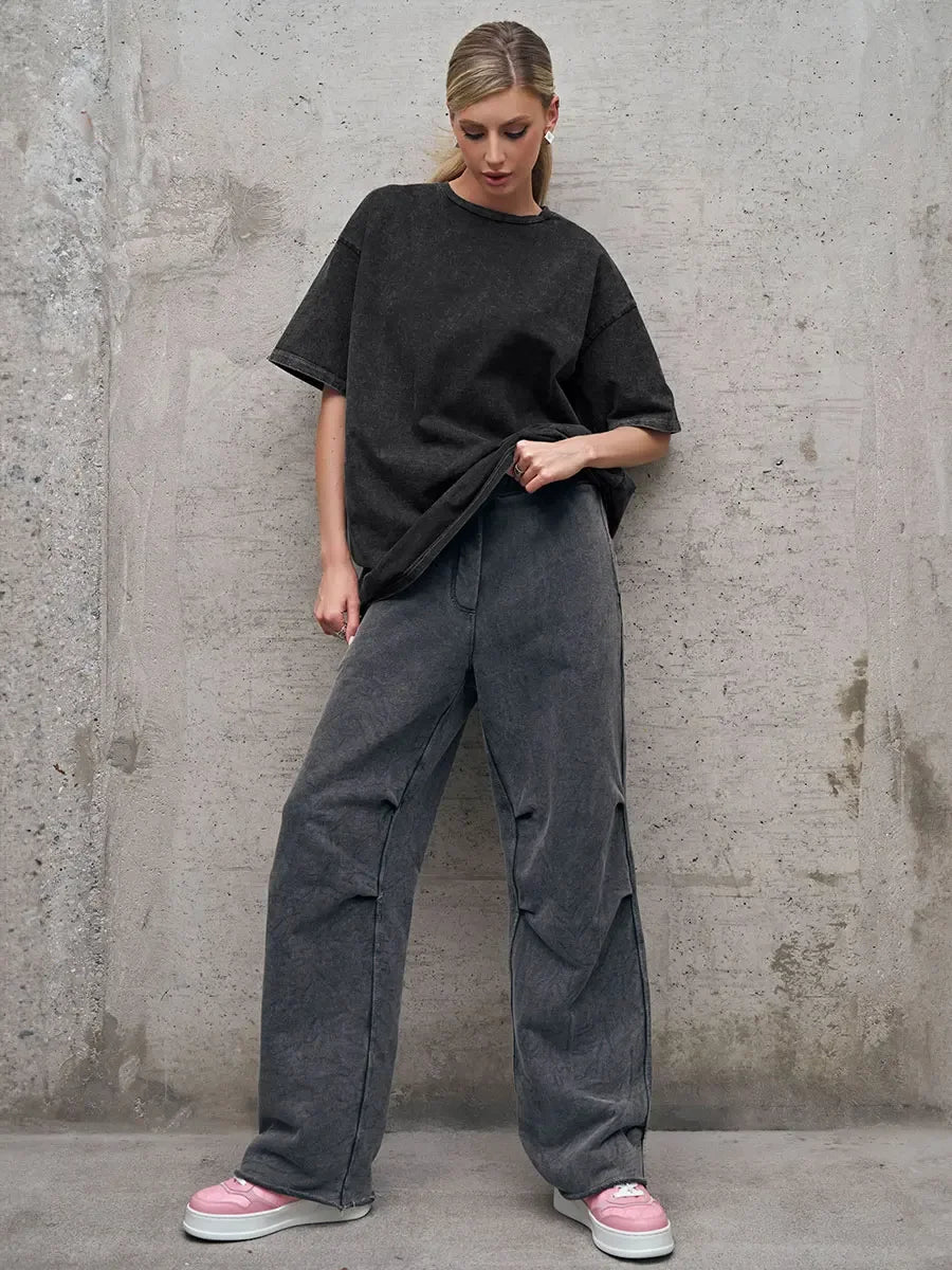 Casual women's outfit featuring a loose black t-shirt and gray wide-leg pants, styled on an urban background.