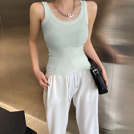 Woman wearing a mint green sleeveless ribbed tank top paired with loose white pants.