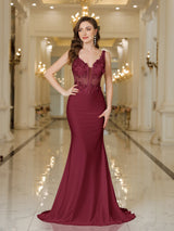 Elegant burgundy evening gown with intricate lace detailing and a fitted silhouette, set in an opulent interior.