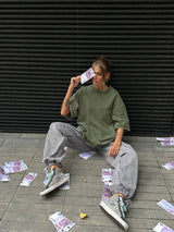 Woman wearing a green oversized t-shirt and gray pants, sitting on the ground with fake money around her.