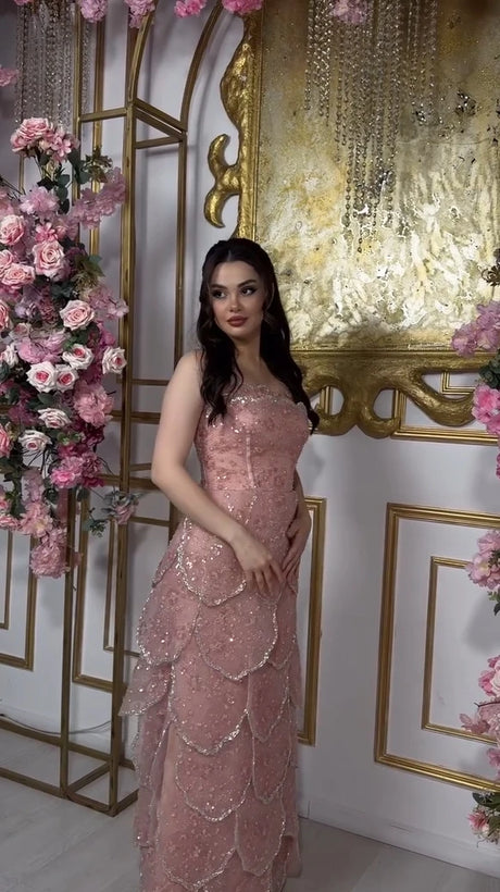 Elegant woman wearing a pink beaded engagement gown with a tiered skirt, surrounded by floral decorations.