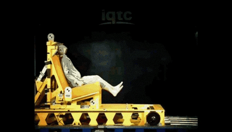 Test simulation of a baby car seat using a crash test dummy on a yellow testing rig with a dark background.