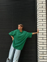 Woman wearing a green oversized casual t-shirt against a textured wall, styled with loose jeans.