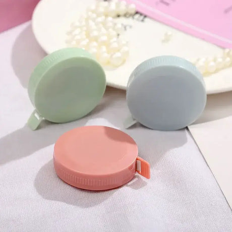 Set of three colorful round measuring tapes in pink, green, and blue on a soft surface, perfect for crafting and sewing.