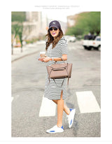 Woman wearing a striped maternity dress with sneakers, holding a coffee cup and a handbag in the city.