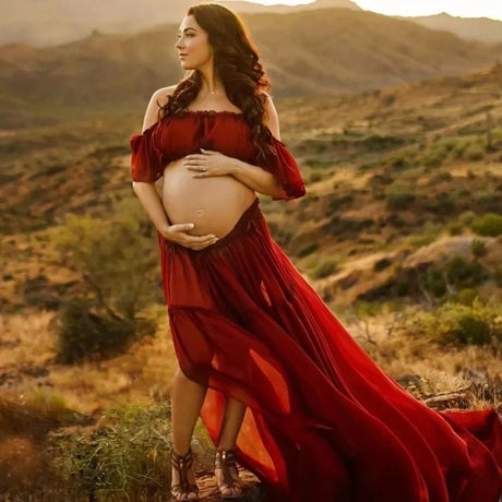 Pregnant woman in a boho two-piece maternity set, posing outdoors in a beautiful red dress at sunset.