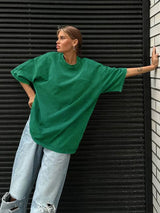 Woman wearing a loose-fitting green casual t-shirt with oversized sleeves against a textured wall.