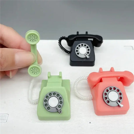 Colorful miniature toy telephones in green, black, and pink, showcasing vintage rotary designs and a detachable receiver.