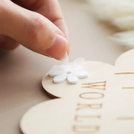 Hand placing a white flower block on a wooden milestone sign for babies, perfect for age tracking.