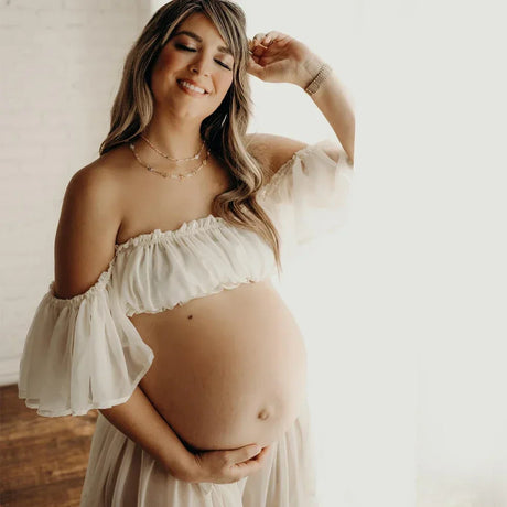 Smiling pregnant woman in a boho two-piece maternity set, showcasing her baby bump during a photoshoot.
