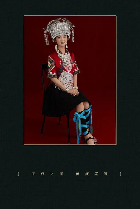 Woman wearing a traditional Miao embroidery suit, seated on a chair with a striking backdrop highlighting festival attire.