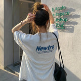 Woman wearing an oversized gray Harajuku streetwear tee with 'Newtro' design in casual urban setting.
