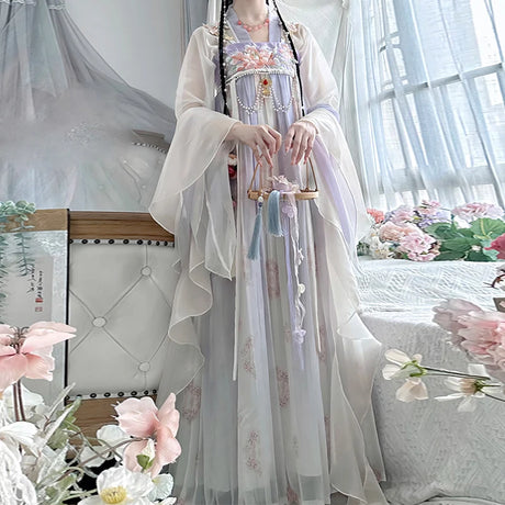 Women in a vintage Chinese Hanfu dress, showcasing delicate floral designs and flowing materials, set in a bright room.