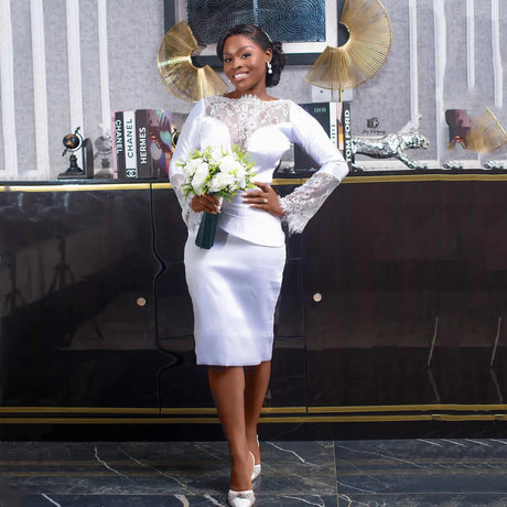 Bridal gown with lace sleeves and tea-length skirt, bride holding bouquet, elegant wedding look in stylish interior.