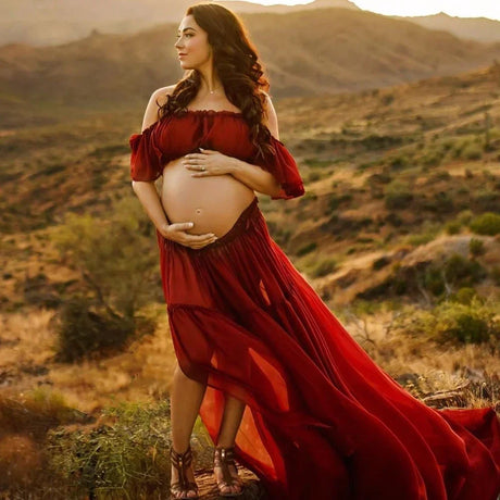 Pregnant woman in a flowing red boho maternity dress in a scenic outdoor setting.