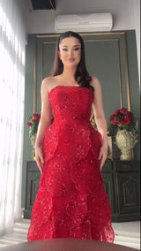 Model wearing a glamorous red strapless evening gown with intricate beading and layered design.